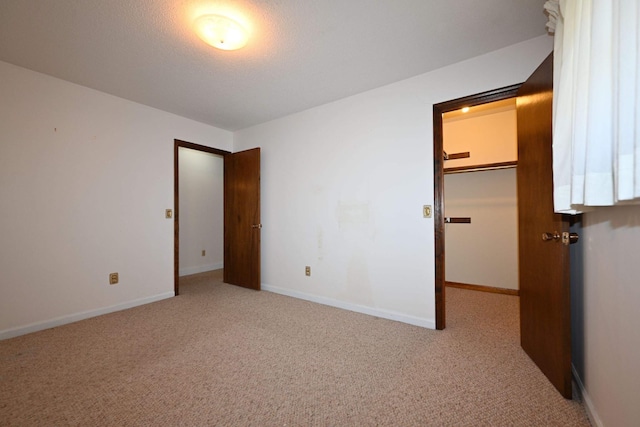 unfurnished bedroom featuring a textured ceiling, light colored carpet, a spacious closet, and a closet