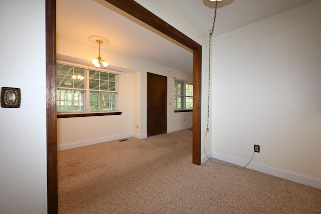 spare room with carpet flooring, a healthy amount of sunlight, and a notable chandelier