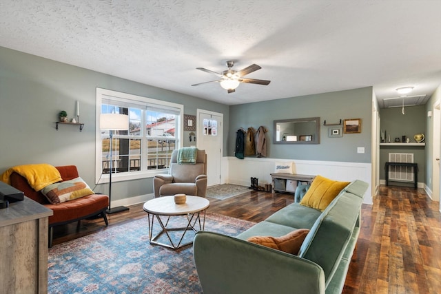 living room with a textured ceiling, ceiling fan, and dark wood-type flooring