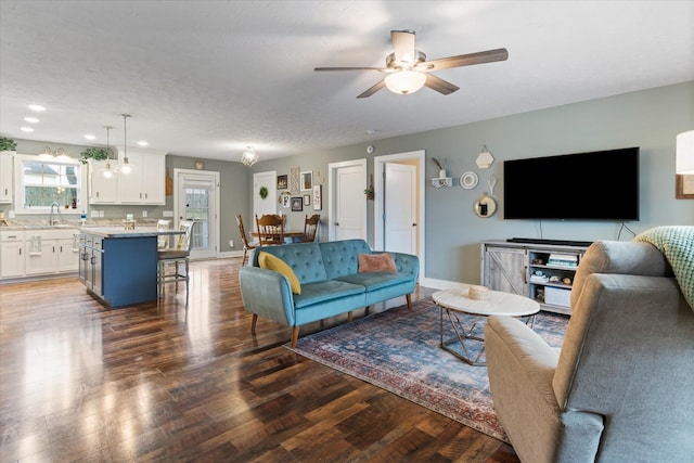 living room featuring a textured ceiling, ceiling fan, sink, and dark wood-type flooring