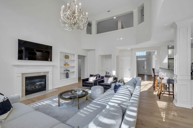 living room featuring a high ceiling, an inviting chandelier, light hardwood / wood-style flooring, built in shelves, and a fireplace