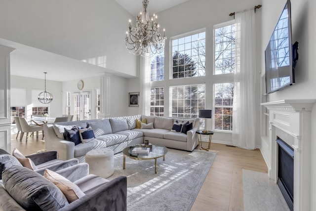 living room with a high ceiling, light hardwood / wood-style floors, ornate columns, and a premium fireplace