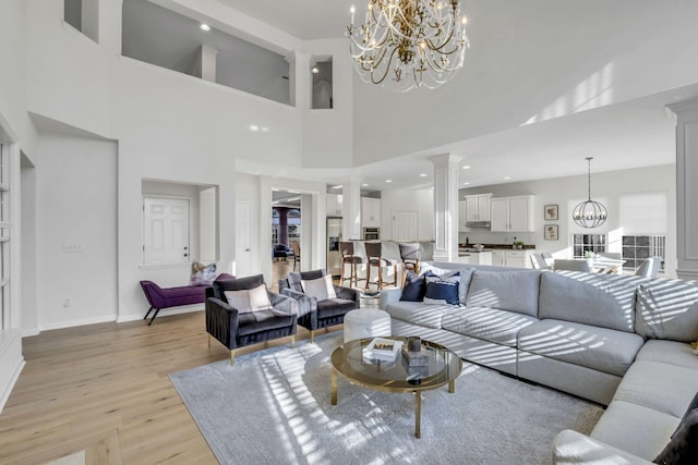 living room featuring a notable chandelier, light wood-type flooring, a high ceiling, and ornate columns