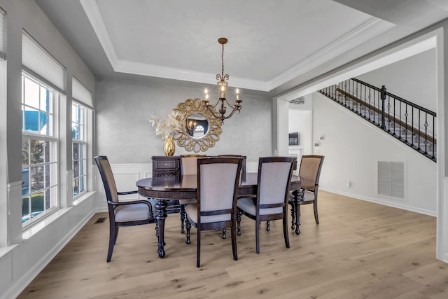 dining area featuring a chandelier, light hardwood / wood-style floors, a raised ceiling, and crown molding