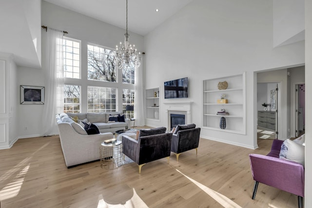 living room featuring a chandelier, light hardwood / wood-style floors, a towering ceiling, and built in features