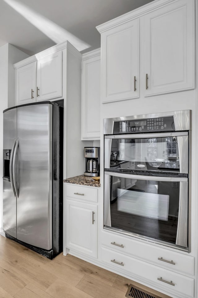 kitchen featuring white cabinets, light hardwood / wood-style floors, appliances with stainless steel finishes, and dark stone counters