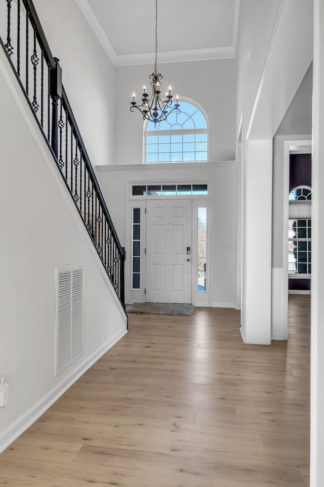 foyer with an inviting chandelier, a towering ceiling, and light hardwood / wood-style flooring