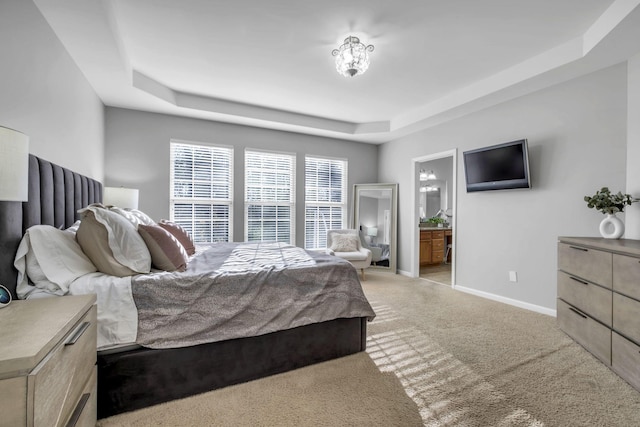 carpeted bedroom featuring a tray ceiling and ensuite bathroom