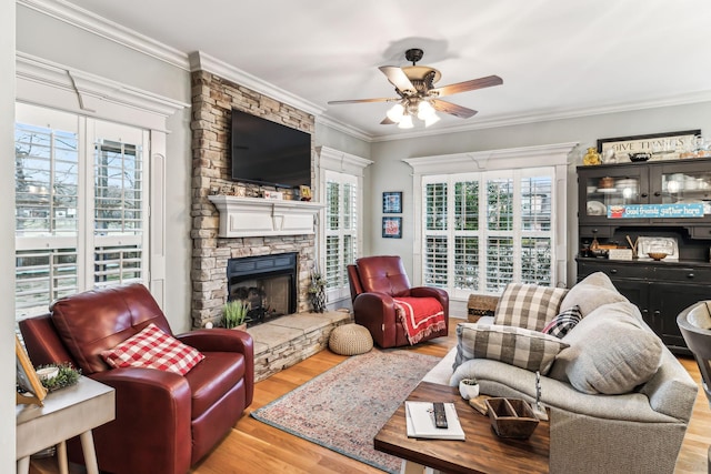 living room featuring hardwood / wood-style flooring, a stone fireplace, ceiling fan, and ornamental molding