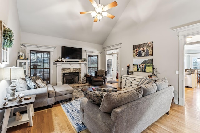 living room featuring ceiling fan, a fireplace, high vaulted ceiling, and light wood-type flooring