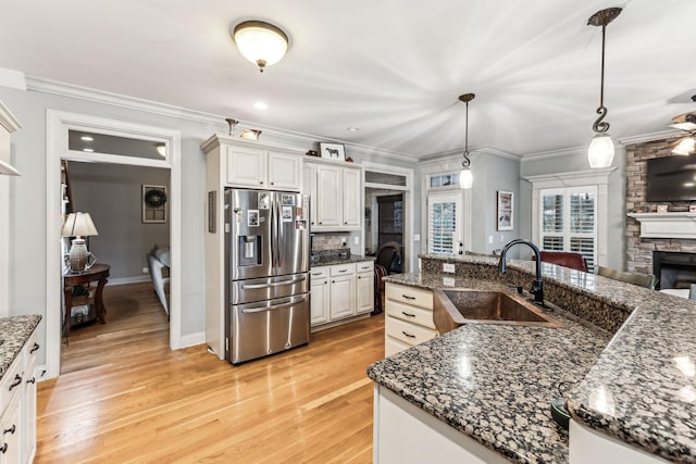 kitchen featuring white cabinetry, sink, hanging light fixtures, a stone fireplace, and stainless steel fridge with ice dispenser