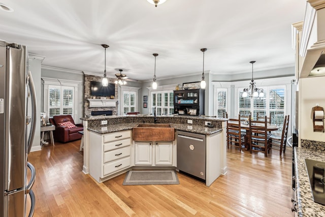 kitchen with a stone fireplace, light hardwood / wood-style flooring, decorative light fixtures, ceiling fan with notable chandelier, and appliances with stainless steel finishes