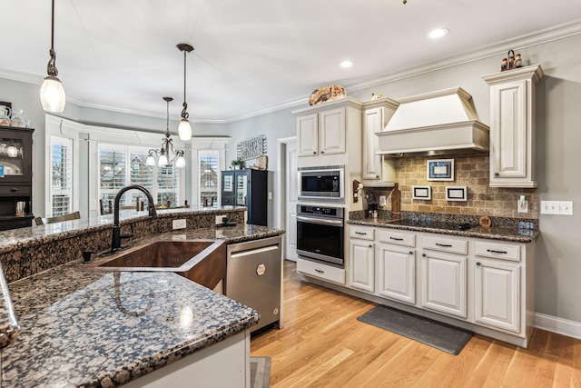 kitchen with appliances with stainless steel finishes, custom exhaust hood, sink, dark stone countertops, and hanging light fixtures