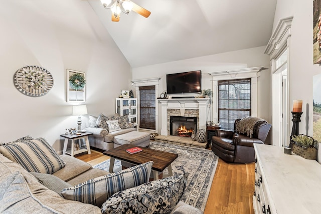 living room featuring ceiling fan, light hardwood / wood-style floors, a stone fireplace, and vaulted ceiling