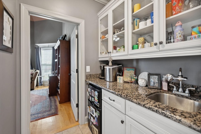 bar featuring dark stone countertops, white cabinetry, sink, and light tile patterned floors