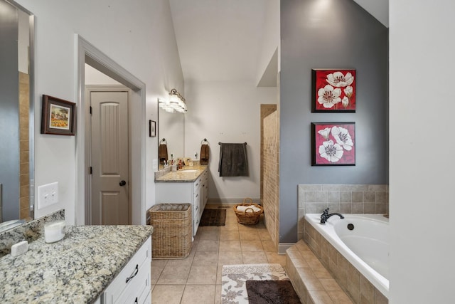 bathroom with tile patterned flooring, vanity, tiled bath, and vaulted ceiling