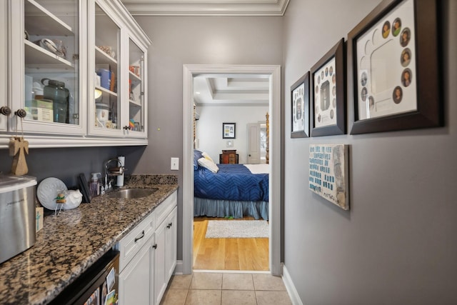 bar with sink, light tile patterned floors, dark stone countertops, crown molding, and white cabinets