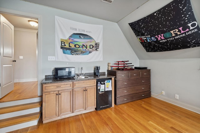 bar with light wood-type flooring, sink, vaulted ceiling, and black appliances