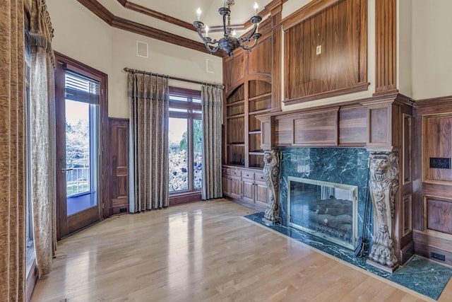 unfurnished living room featuring an inviting chandelier, light hardwood / wood-style flooring, a wealth of natural light, and ornamental molding