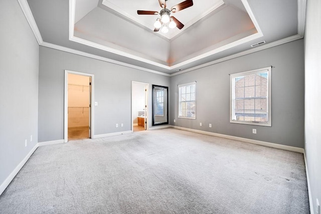 unfurnished bedroom featuring a walk in closet, a tray ceiling, ceiling fan, and crown molding