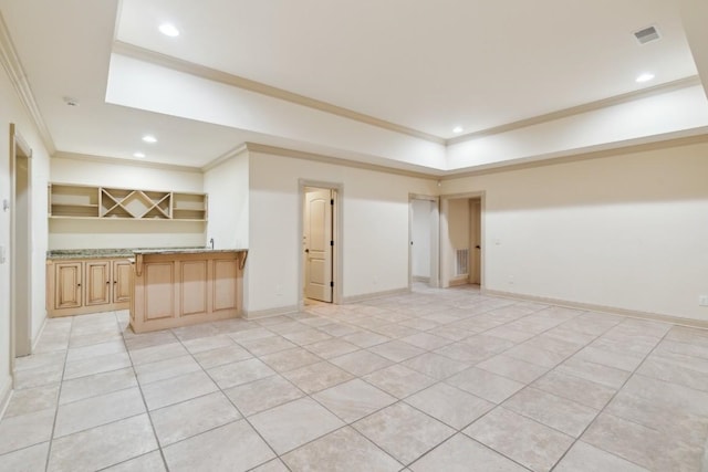 interior space with light tile patterned floors, a raised ceiling, ornamental molding, and bar area