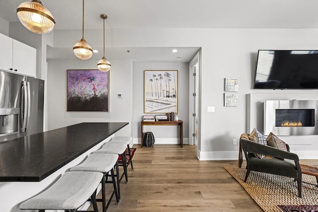 kitchen featuring white cabinetry, hanging light fixtures, stainless steel refrigerator with ice dispenser, a breakfast bar, and hardwood / wood-style flooring