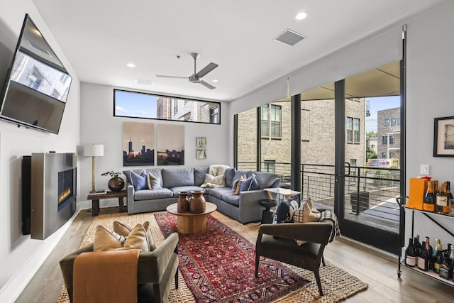 living room featuring light hardwood / wood-style flooring, ceiling fan, and a healthy amount of sunlight