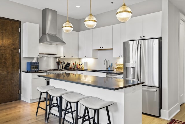 kitchen featuring stainless steel appliances, wall chimney range hood, white cabinets, light hardwood / wood-style floors, and hanging light fixtures