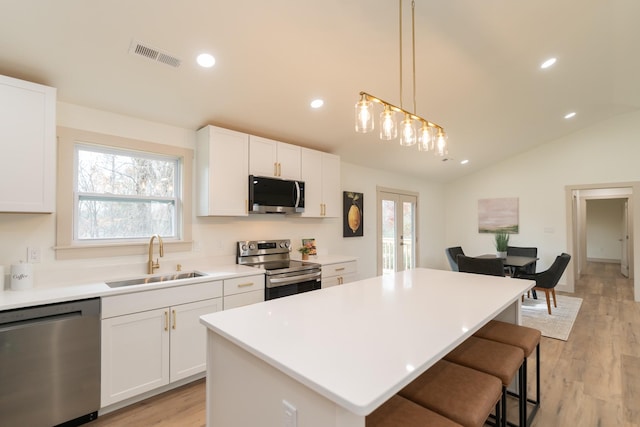 kitchen with white cabinetry, sink, a center island, stainless steel appliances, and lofted ceiling