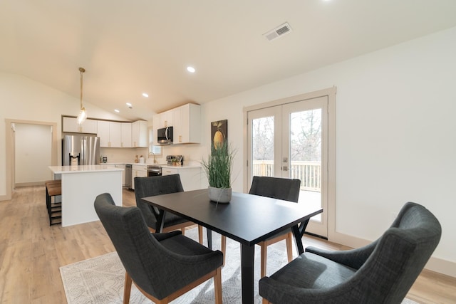 dining area with light hardwood / wood-style floors, french doors, and vaulted ceiling