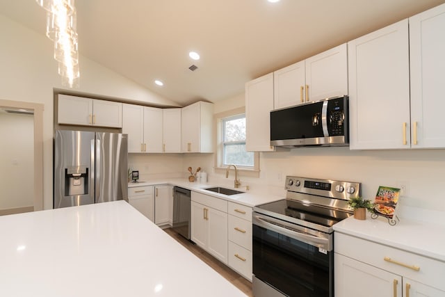 kitchen with appliances with stainless steel finishes, white cabinetry, vaulted ceiling, and sink