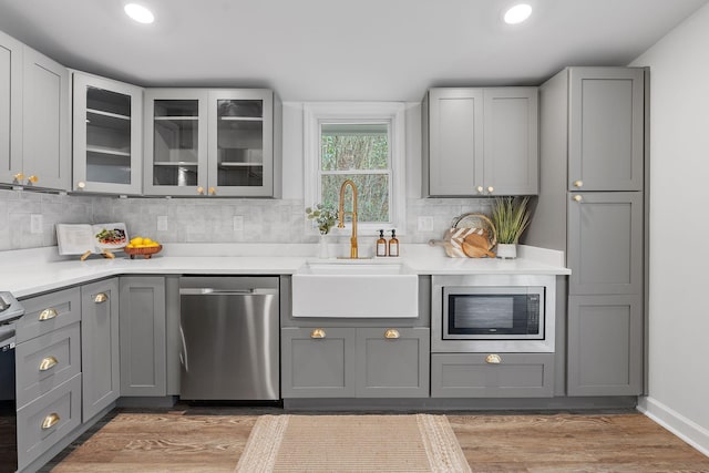 kitchen featuring gray cabinetry, backsplash, sink, light hardwood / wood-style flooring, and stainless steel appliances