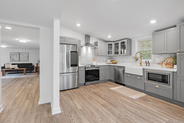 kitchen featuring gray cabinets, wall chimney range hood, appliances with stainless steel finishes, and light hardwood / wood-style flooring