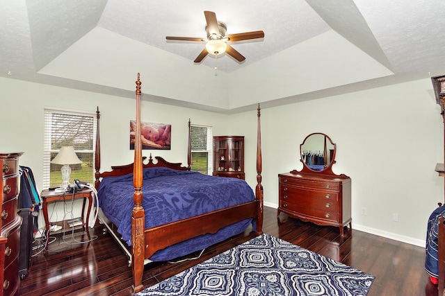 bedroom with dark hardwood / wood-style floors, ceiling fan, and a tray ceiling