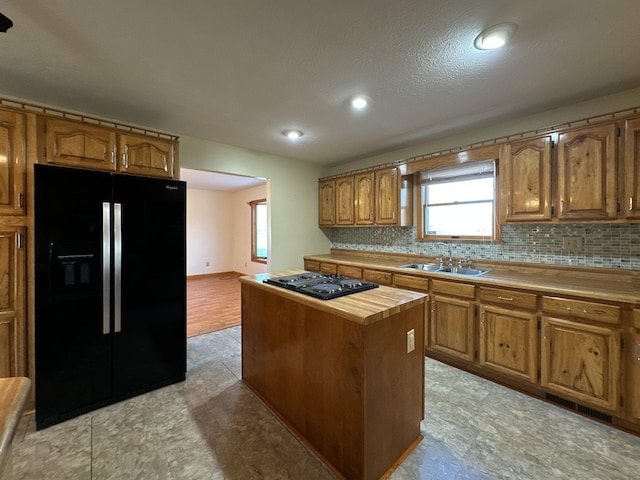 kitchen featuring black appliances, sink, a textured ceiling, tasteful backsplash, and a kitchen island