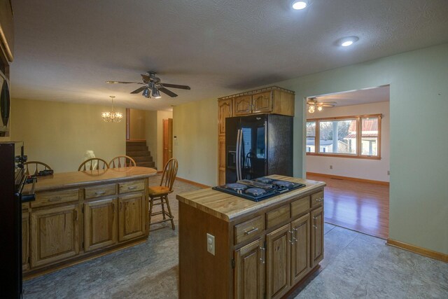 kitchen featuring black appliances, ceiling fan with notable chandelier, a kitchen island, and a textured ceiling