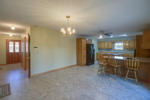 kitchen with a kitchen bar, decorative backsplash, kitchen peninsula, black fridge with ice dispenser, and ceiling fan with notable chandelier