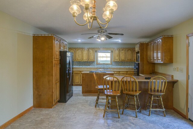 kitchen with sink, kitchen peninsula, a breakfast bar area, black appliances, and ceiling fan with notable chandelier