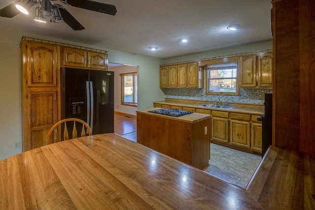 kitchen with light wood-type flooring, a healthy amount of sunlight, sink, black appliances, and a center island