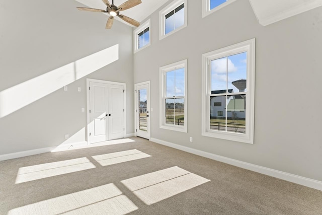 unfurnished living room with carpet flooring, ceiling fan, crown molding, and a towering ceiling