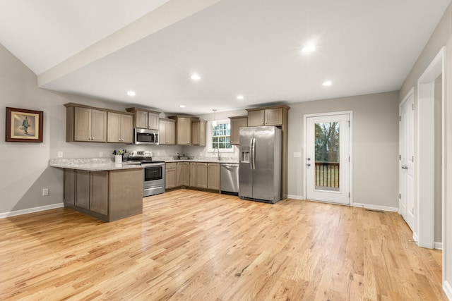 kitchen featuring kitchen peninsula, appliances with stainless steel finishes, light wood-type flooring, vaulted ceiling, and hanging light fixtures