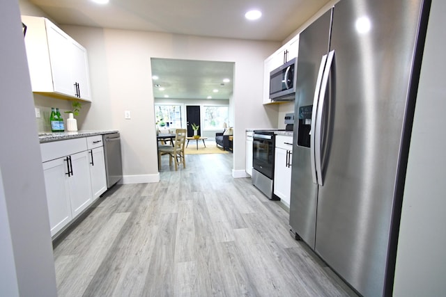 kitchen featuring white cabinets, appliances with stainless steel finishes, light hardwood / wood-style flooring, and light stone countertops