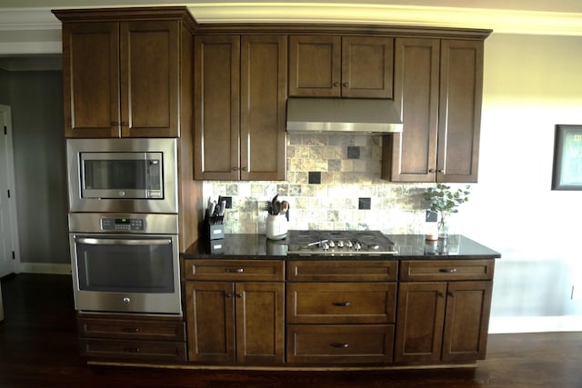 kitchen featuring tasteful backsplash, stainless steel appliances, crown molding, dark stone countertops, and dark hardwood / wood-style floors