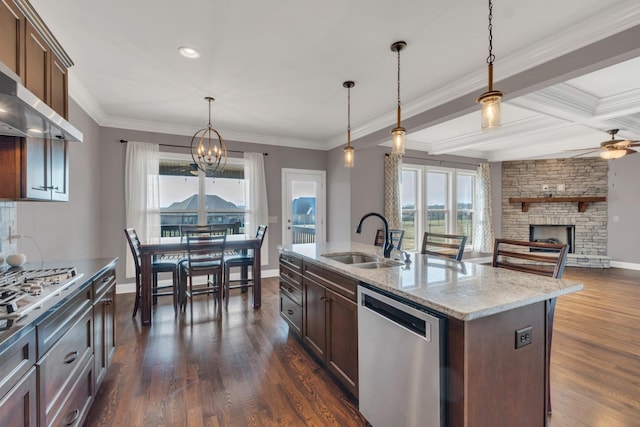 kitchen with dark wood finished floors, appliances with stainless steel finishes, a stone fireplace, wall chimney range hood, and a sink