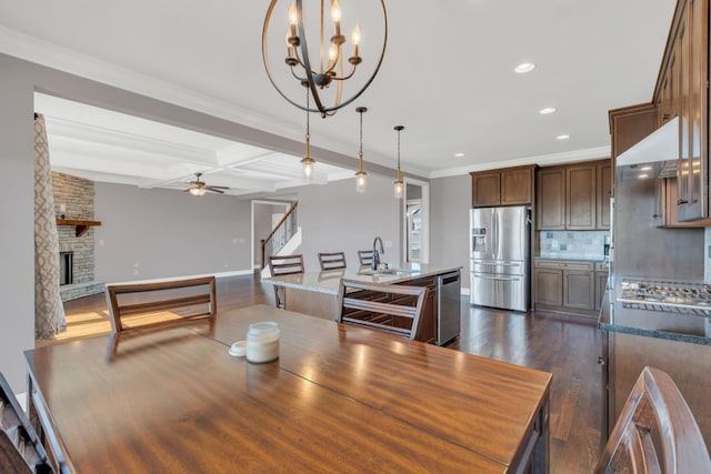 dining space with dark wood-style floors, crown molding, a fireplace, beamed ceiling, and ceiling fan with notable chandelier