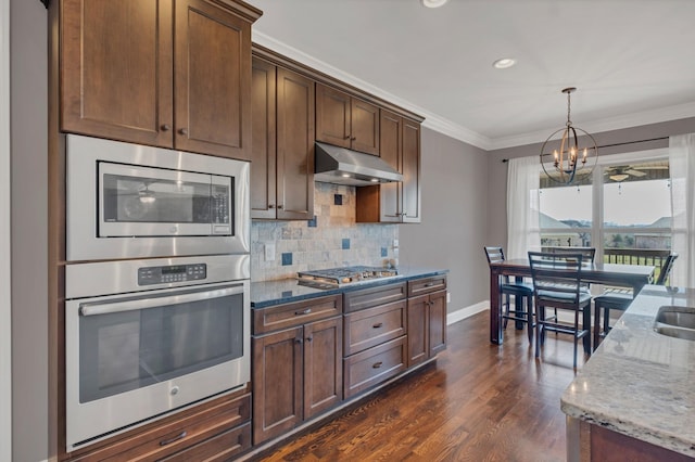 kitchen with decorative backsplash, appliances with stainless steel finishes, light stone countertops, crown molding, and under cabinet range hood