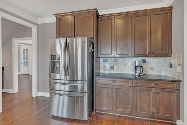 kitchen featuring crown molding, decorative backsplash, dark stone countertops, and stainless steel fridge with ice dispenser