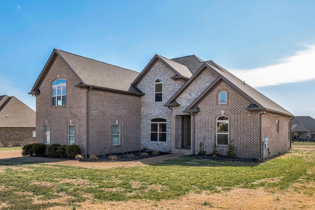 view of front facade with stone siding, brick siding, a front yard, and a shingled roof