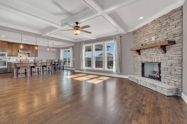 living area featuring ornamental molding, dark wood finished floors, beamed ceiling, and a stone fireplace