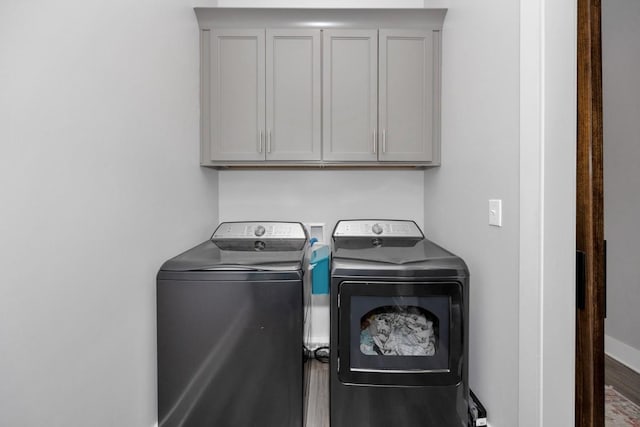 clothes washing area with washer and dryer, cabinets, and wood-type flooring